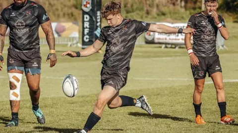 A young rugby player in a black strip prepares to kick the ball in a game