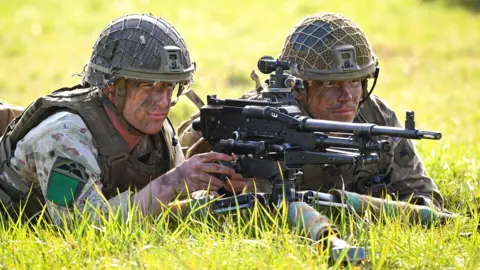 British Soldiers in full combat uniform lying on grass pointing an automatic rifle at a target out of shot during a training exercise .