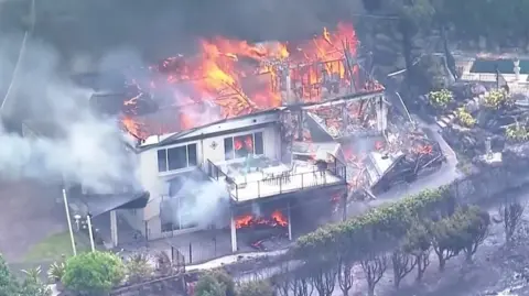 A house on fire engulfed by smoke and flames.