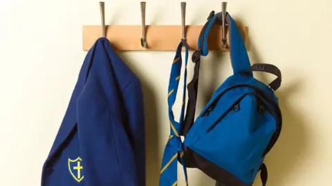 Getty Images A blue blazer, yellow and blue tie and blue backpack hanging on hooks.