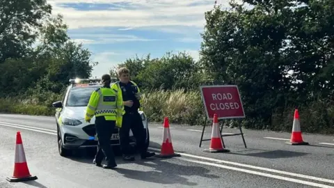 Dan Jessup A police car and cones block the road, with a 'Road Closed' sign