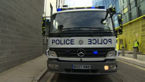 A large truck with Police on the front and blue lights flashing