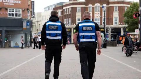 Charnwood Borough Council The backs of two street security staff wearing blue and black uniforms - in Loughborough town centre
