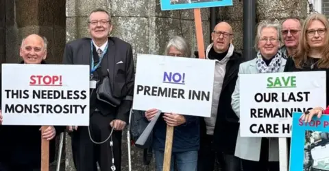 LDRS A group of six people, some holding protest banners. One reads "Stop this needless monstrosity"