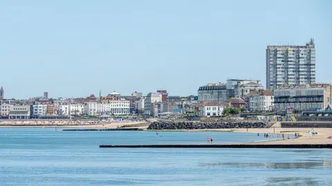 Getty Images The bay in Margate on a sunny day. The sea appears still, there are people on the beach and in the water, and the town's seafront buildings can be seen. A large concrete building towers over the rest of the town.