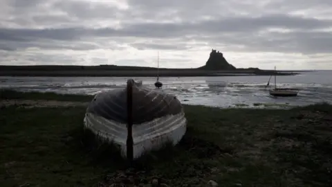 An overturned boat on the Holy Island shore, with the castle viewable in the background