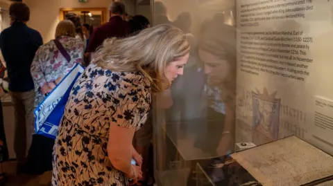 Durham Cathedral A blonde haired woman looks down at a copy of the Magna Carta behind a display case.