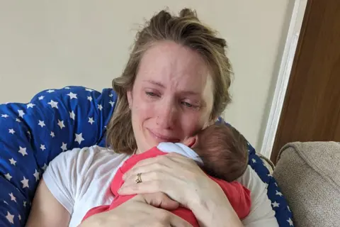 Louise cuddles her newborn baby, while she is crying