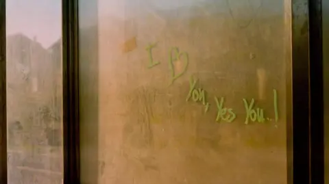 Archie Byron The image shows a dirty phone box with the words "I love you, yes you!" written in pen on the window.