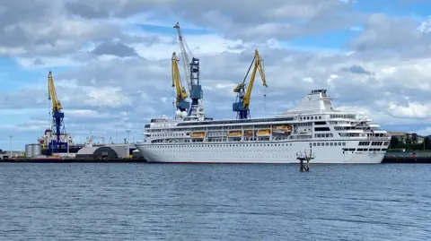 White cruise ship, surrounded by yellow cranes in the docks. 