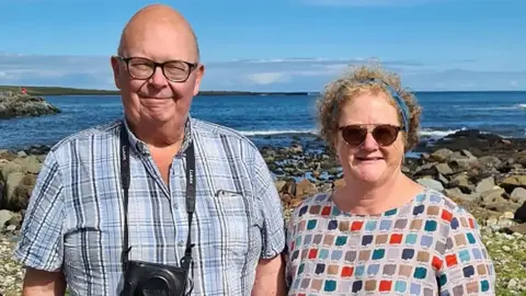 Martin and Jo Cousland, pictured on a rocky beach on a sunny day.