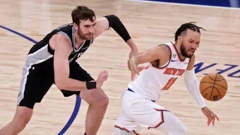 The San Antonio Spurs' Luke Kornet chases the New York Knicks' Jalen Brunson