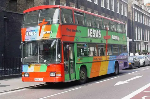 British Museum A brightly-coloured Jesus Army bus parked outside a row of terraced houses in London