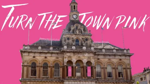 Ipswich Central A view of Ipswich's Town Hall against a pink backdrop. The words 'Turn the town pink' are written in a white font around the hall.