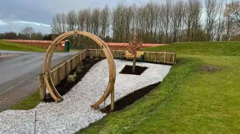 Carlisle United Carlisle United's memorial garden which has a hoop as an entrance with a tree at its centre surrounded by white gravel and a bed of plants to one side with a low wicker fence around it 