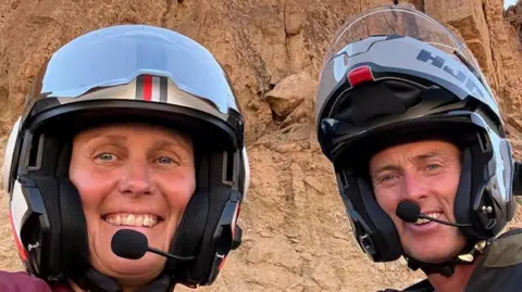 PA Media Lindsay and Craig are seen beaming in motorcycle helmets in a selfie picture