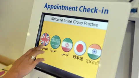 PA A woman's hand presses a touch screen to access a GP appointment