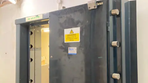 A black bank vault door with a yellow warning sign on the front