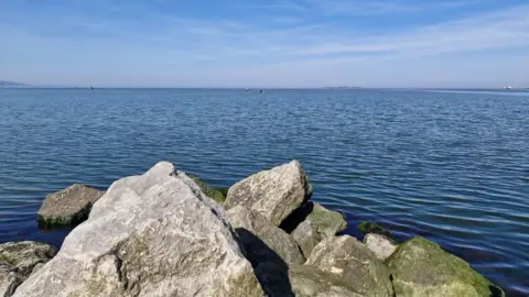 A wide shot picture of the sea with rocks at the front of the shot