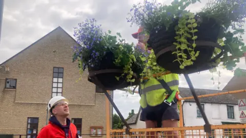 Mousumi Bakshi/BBC Hanging baskets being put up.