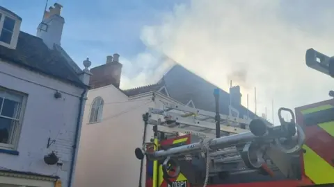 DWFRS Back of fire engine with cream building in background with smoke coming from the roof