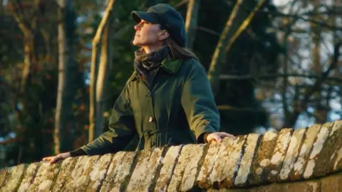 Princess of Wales leans on a stone wall on a bridge in a coat on a walk in the countryside