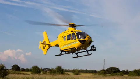 Graham Eva bright yellow helicopter hovers over a green field