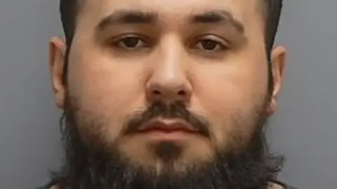 A custody shot of Rrahim Statovci, a man with short hair and a large beard. 