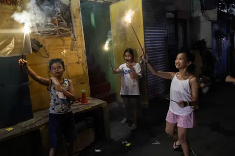 Eloisa Lopez/REUTERS Crianças acendem fogos de artifício durante as celebrações do Ano Novo em uma rua na cidade de Mandaluyong, região metropolitana de Manila, Filipinas, em 31 de dezembro de 2024. 