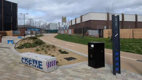 A view of a footpath with a concrete bench with the word Crewe on it.