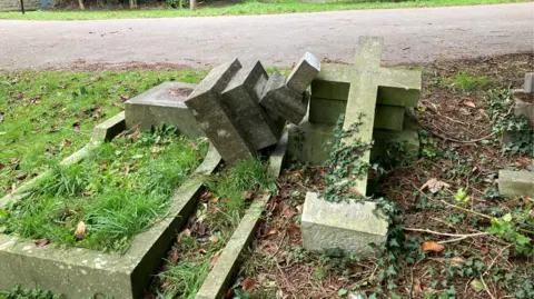 BBC Two graves next to each other with a large tombstone resembling a cross appearing to have been knocked off the left hand grave on to the one on the right