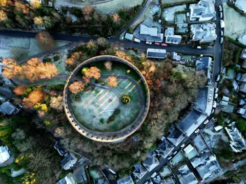 Robert Kitchen A top down aerial view of McCaig’s Tower in Oban, with greenery and other homes and buildings also visible around it.