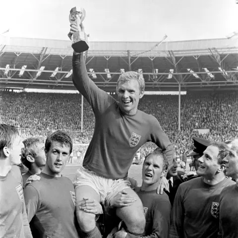 PA Media England's triumphant 1966 World Cup final captain Bobby Moore chaired by hat-trick hero Geoff Hurst (L) and Ray Wilson as he salutes the crowd with the Jules Rimet Trophy after the 4-2 victory against West Germany at Wembley