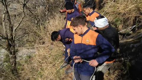 @HP_SDRF/X Rescue workers wearing blue and orange fleeces hold ropes as they work to tether the stretcher to the mountain