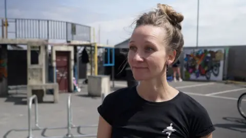 Shaun Whitmore/BBC Anja Meinhardt wears a black top and looks slightly ahead of the camera. She has a smile on her face and her hair is up in a bun. She is standing in a playground