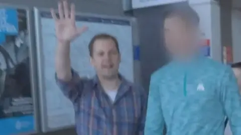 A screengrab of Robert Jenrick holding up his hand as he confronts a fare dodger, whose face is blobbed out, at a Tube station.