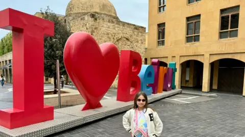 SUPPLIED Dan Harper's daughter standing next to a Beirut city landmark that reads I love Beirut