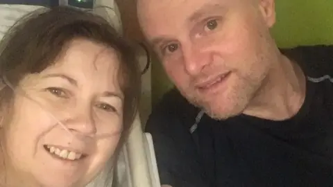 Family A woman is on the left of the photo and a man wearing a dark top is on the right in front of a green background.