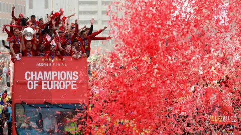 Reuters Red confetti in the air in front of the Liverpool bus in 2019. Players raise their arms in celebration on the open-top bus.