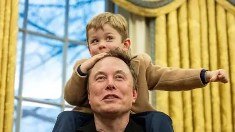 Elon Musk's son, X, sits on his shoulders in the Oval Office