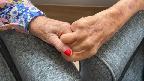 A close up image of Terry and Jean holding hands on the sofa