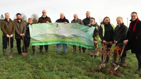 SUPPLIED A group of people stood in grass holding up a sign