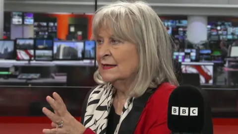 Headshot of Baroness Kennedy speaking in a BBC studio. She wears a red jacket with a black and white silk scarf. 