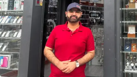 Ibrahim Faheed stood outside his shop wearing red shirt and blue cap
