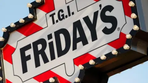 A TGI Fridays sign, with the font in black surrounded by white and red stripes and light bulbs.