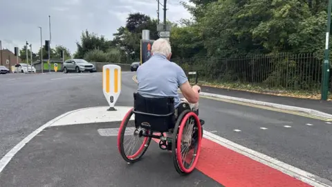 Man in a wheelchair on a crossing waiting to go over to the pavement