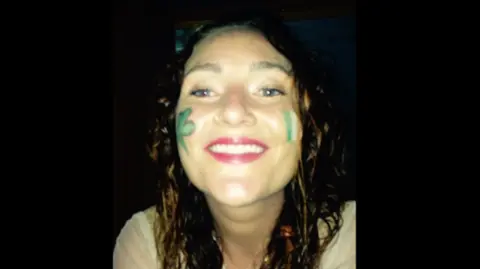 PA A woman smiles into the camera. She has face paint on her cheeks of a shamrock and a tricolour flag. 