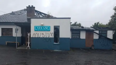 Building with roof burnt out and "Muslim out" spray painted twice on wall