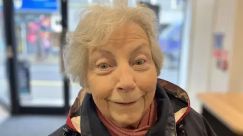 And older person with grey hair smiling at the camera with large happy eyes