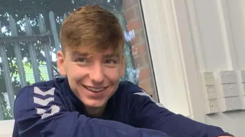 PA Media Close up of Adam Ankers, who had dark blond hair swept forward on his forehead. He is smiling and looking in the distance beyond the camera